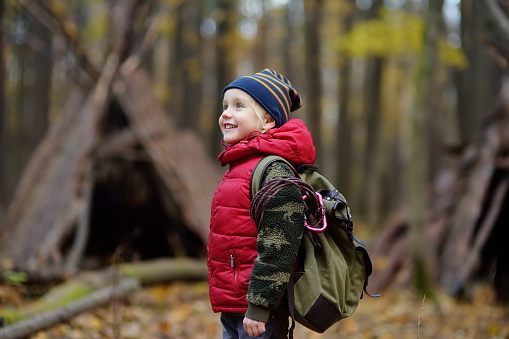 Little boy scout during hiking in autumn forest. Teepee hut on background.