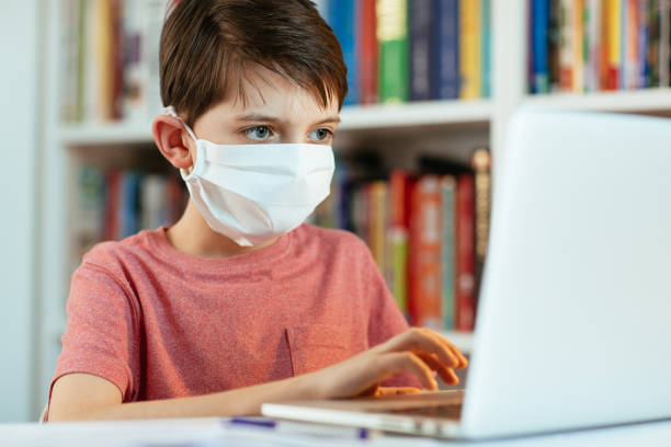 Child wearing face mask learning at home during virus time. stock photo