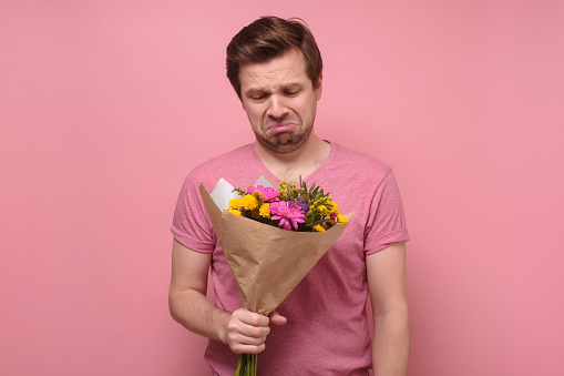 Triste amante o hombre de corazón roto en ropa rosa de pie con ramo de flores.a photo