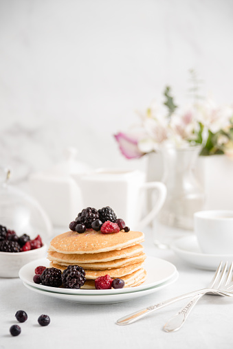PancPancakes with berries and honey on the plate. White white background