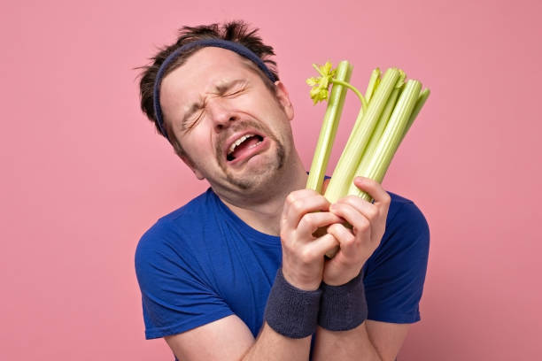 man holding celery crying. I hate vegetables but should eat for healthy diet. Funny handsome sporty man with mustache holding fresh celery crying. I hate vegetables but should eat for healthy diet. Studio shot on pink wall eating body building muscular build vegetable stock pictures, royalty-free photos & images