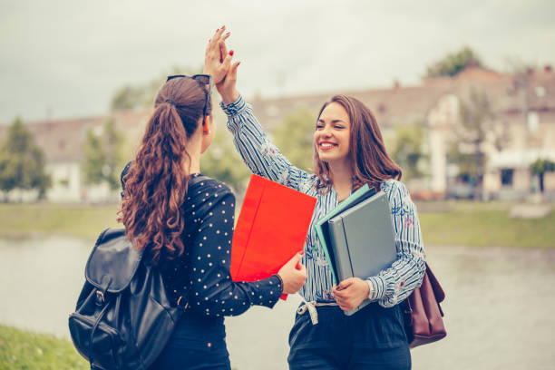 istock Happy Female students giving five to each other during friendly collaboration on studying project, while standing outdoor 1213365749