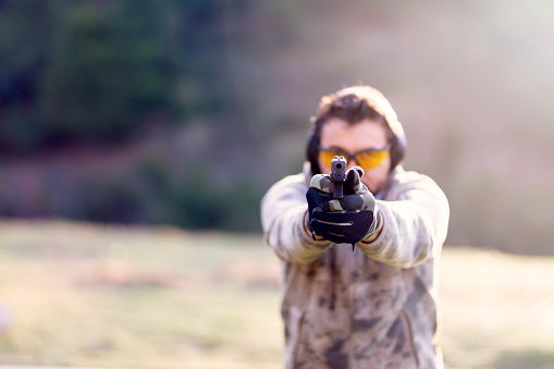 Shooter holding gun in hand and shooting. Close-up detail