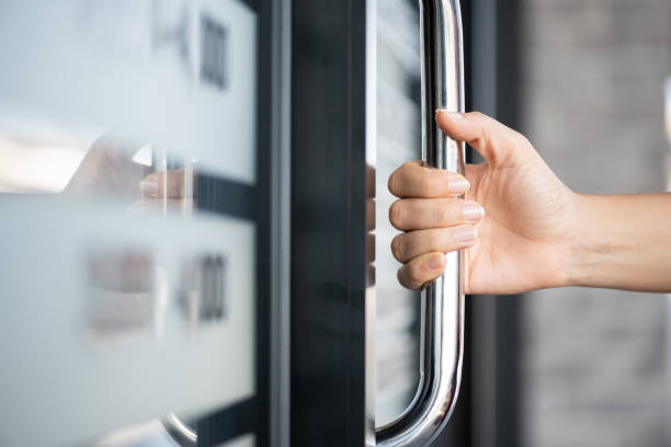 de hand die van de close-upvrouw de deurstaaf houdt om de deur met glasbezinningachtergrond te openen. - deurknop stockfoto's en -beelden