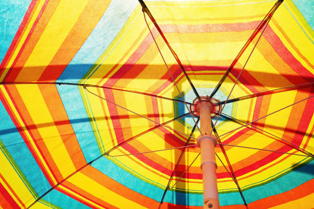 textura de una colorida sombrilla de playa abierta con rayos translúcidos del sol de verano. viajes y turismo. descanso y vacaciones - rainbow umbrella descriptive color multi colored fotografías e imágenes de stock