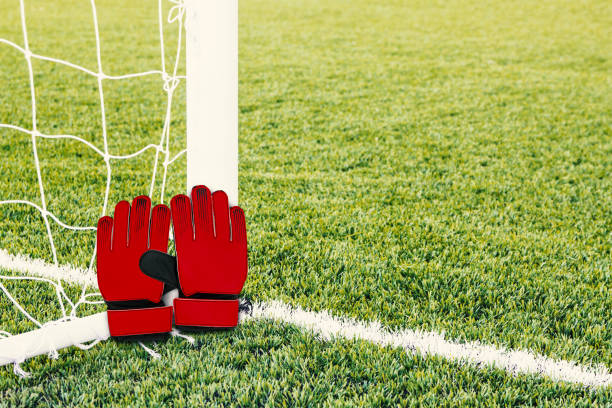 Red goalkeeper gloves with soccer goal background.