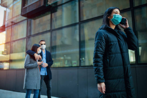 Young girl wearing a protective mask in the city talking on a phone. Group of people using telephone wearing pollution masks. stock photo