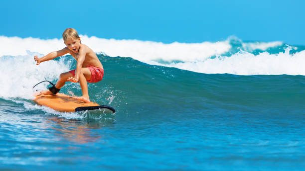 Young surfer learn to ride on surfboard on sea waves Happy baby boy - young surfer learn to ride on surfboard with fun on sea waves. Active family lifestyle, kids outdoor water sport lessons, swimming activity in surf camp. Summer vacation with child. raro stock pictures, royalty-free photos & images