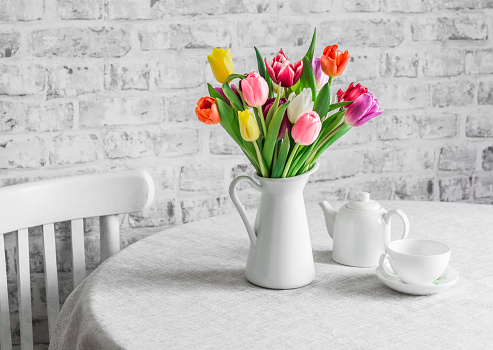 Bouquet of tulips , teapot and teacup on the table in the bright kitchen. Cozy home concept