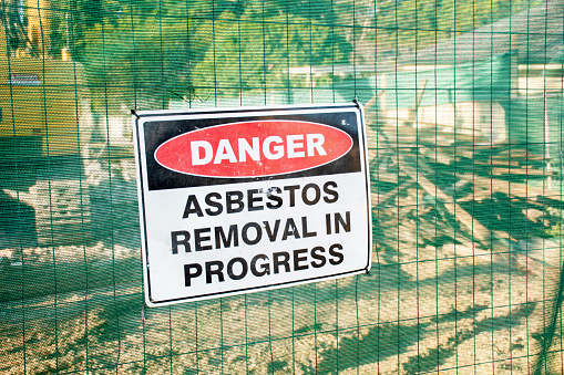 A warning sign Danger Asbestos on a fence at construction site where old house is demolishing