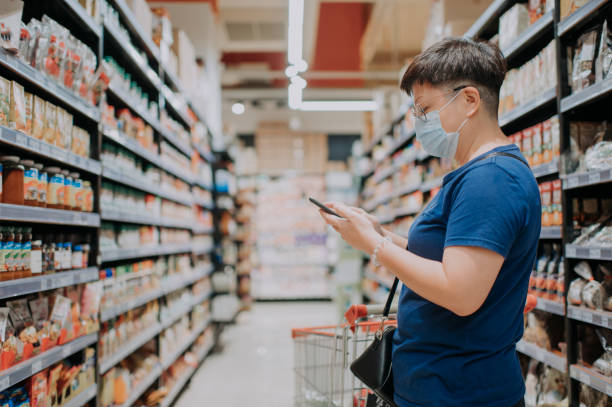 an asian chinese female wearing a mask going out shopping in supermarket looking at phone checking list - asian ethnicity shopping mall supermarket store imagens e fotografias de stock