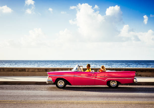 kubanischer fahrer nimmt einen touristen auf einer stadtrundfahrt in einem amerikanischen roten cabrio oldtimer auf der promenade malecon in havanna city cuba - serie cuba reportage - 1950 1959 stock-fotos und bilder