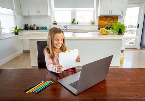 Coronavirus Outbreak. Lockdown and school closures. Schoolgirl watching online education class, happy talking with teacher on the internet at home. COVID-19 pandemic forces children online learning.