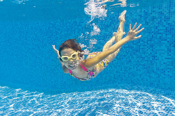 A smiling child swimming underwater in a pool in goggles
