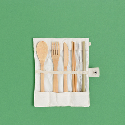 Set of bamboo cutlery in a case on a green pastel background. Zero waste concept.