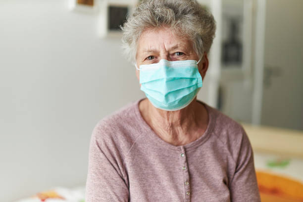 um idoso se senta sozinho em sua cama com um respirador ou máscara cirúrgica - senior citizen woman - fotografias e filmes do acervo