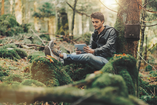 Young handsome man using a digital tablet in the forest and relaxing