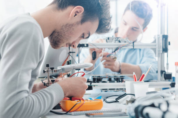 Engineering students working in the lab Engineering students working in the lab, a student is using a voltage and current tester, another student in the background is using a 3D printer 3d printing lab stock pictures, royalty-free photos & images