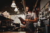Cheerful young caucasian cafe owner wearing apron using digital tablet