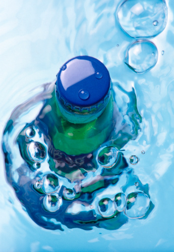 Green bottle with green cap under water with bubbles, directly above.