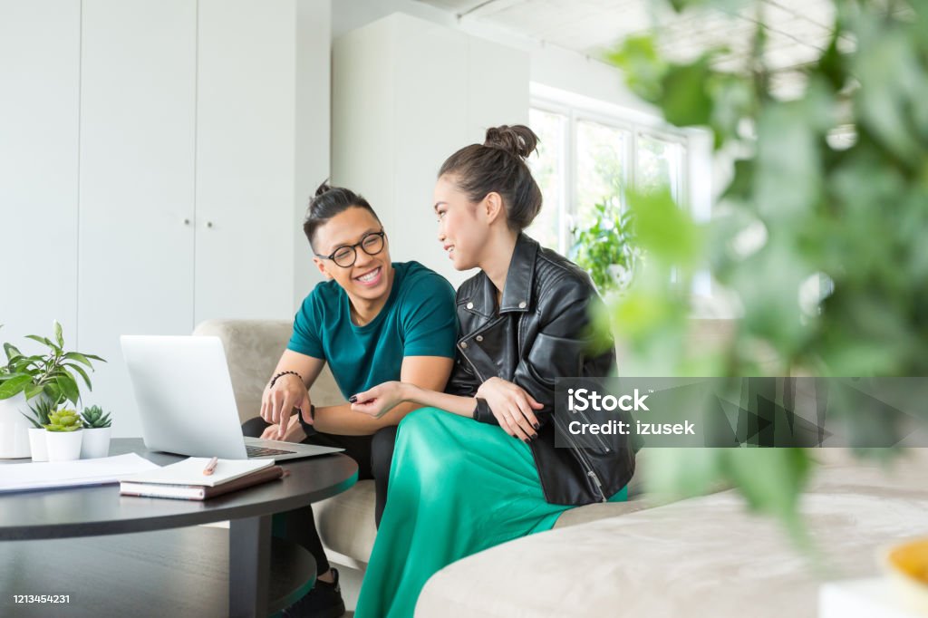 Colleagues working together on laptop in the office Asian entrepreneurs discussing over laptop at table. Male and female graphic designers sitting at creative workplace. They are in smart casuals in office. Business Casual Stock Photo