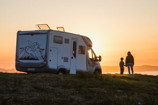 mother and child watching a sunset over the sea, traveling in the motor home