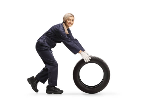 istock Female auto mechanic rolling a tire and smiling at the camera 1213458740