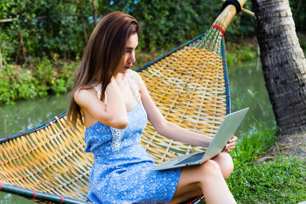 istock Young pretty woman sitting in bamboo hammock using laptop 1213458956