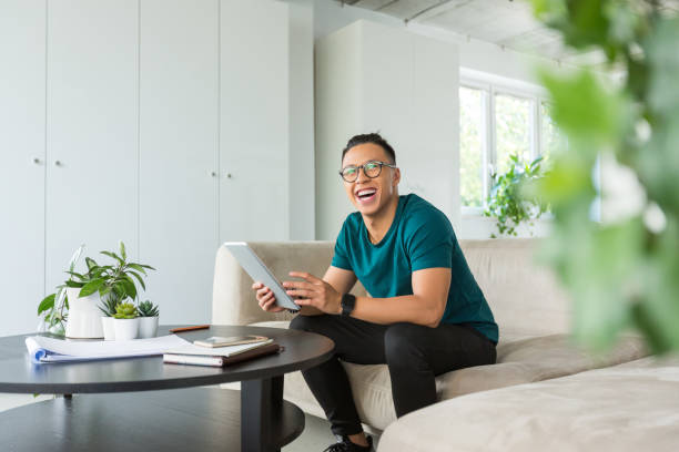 jeune homme de sourire travaillant sur la tablette numérique dans le bureau - cheerful business person strategy people photos et images de collection