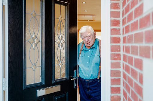 Senior man opening his front door to see who is there. He is looking at the camera curiously