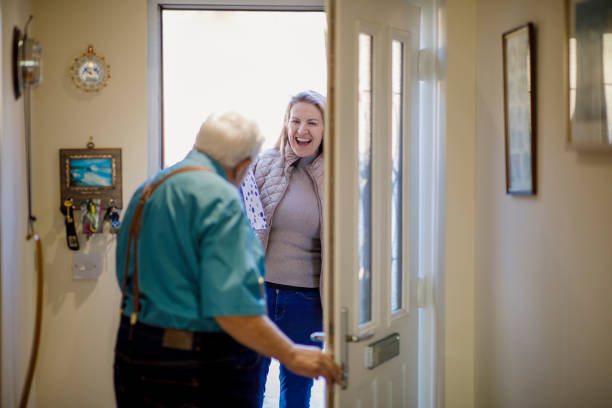 Well Hello! Caucasian senior male opening the front door to his daughter holding a gift. father daughter 80s stock pictures, royalty-free photos & images