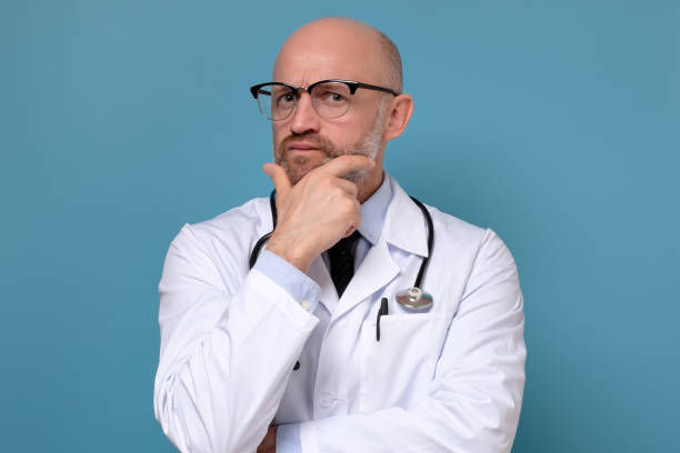 istock Serious mature doctor man thinking standing with arms folded 1213465108