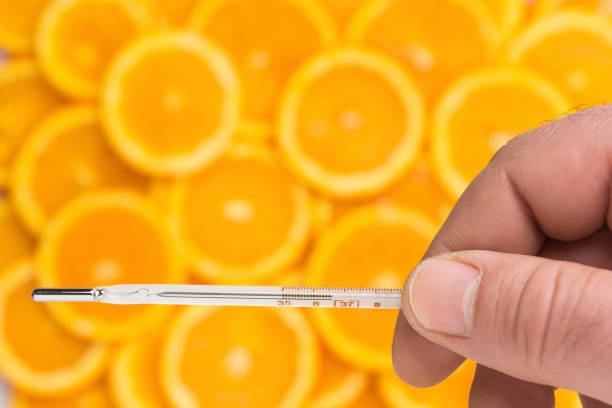 la main cultivée tient un thermomètre au mercure au-dessus d’un modèle de tranches d’orange fraîche comme un concept de supplément de nutrition contre la grippe - thermometer cold fever focus photos et images de collection