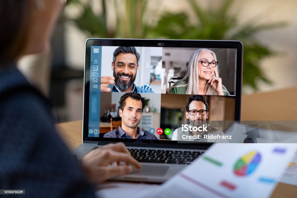 Smart working and video conference Back view of business woman talking to her colleagues about business plan in video conference. Multiethnic business team using laptop for a online meeting in video call. Group of businessmen and businesswomen smart working from home. Video Conference Stock Photo
