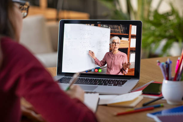 Studying with video online lesson at home Young student watching lesson online and studying from home. Young woman taking notes while looking at computer screen following professor doing math on video call. Latin girl student studying from home and watching teacher explaining math formula on video chat. teach online stock pictures, royalty-free photos & images