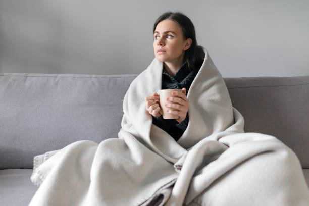 istock Young woman with cup, sitting at home on sofa 1213470786
