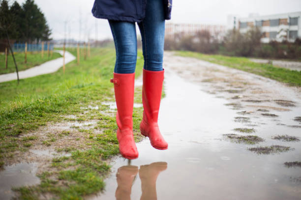 istock Girl in rubber boots is jumping into a big puddle 1213471624