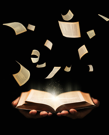 Man is holding book with flying pages and radiance light on black background. learing, reading, knowledge concept