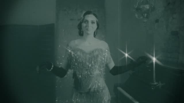 Old 20s black and white film with grain. Happy beautiful young flapper woman smiling in bright sparkling silver dress. roar fluttering gown. laughs dances in vintage retro room, piano, candles burning