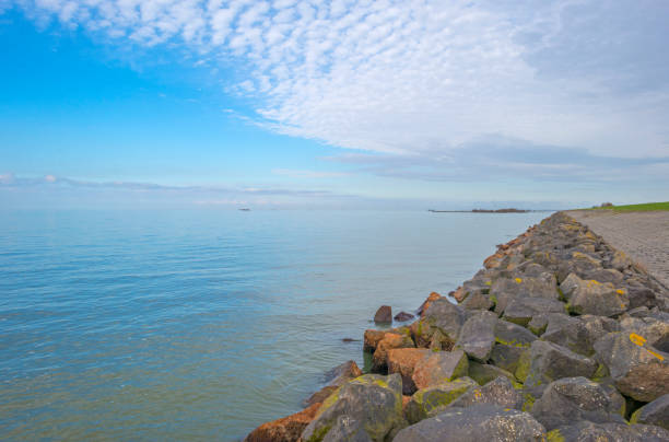 istock Dike along a lake in sunlight below a blue cloudy sky in winter 1213474619