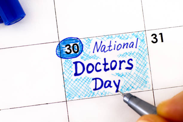 Woman fingers with pen writing reminder National Doctors Day in calendar. March 30. stock photo