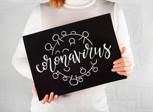 Woman keeps a chalkboard with a drawn and inscription of CORONAVIRUS Woman keeps in hands a black chalkboard with a drawn and inscription of CORONAVIRUS the human body writing black human hand stock pictures, royalty-free photos & images