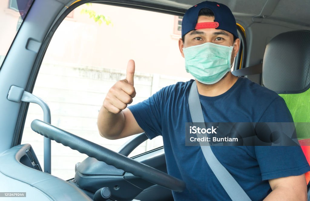Truck driver wearing a mask Close-up photos of Asian truck drivers wearing masks to protect against dust and the spread of the flu. Covid 19. Inside the car front Essential Services Stock Photo