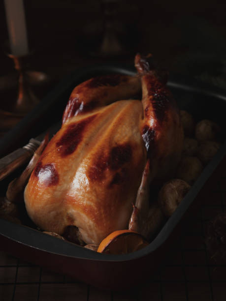 istock Whole roasted chicken with lemon and potatoes in casserole dish on dark background. 1213480131