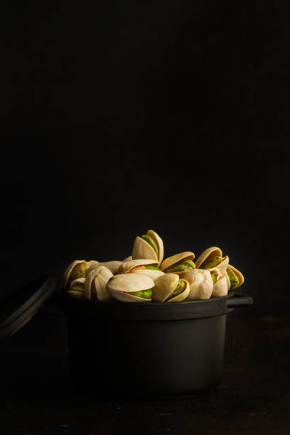 Green pistachios in a black bowl on a dark background