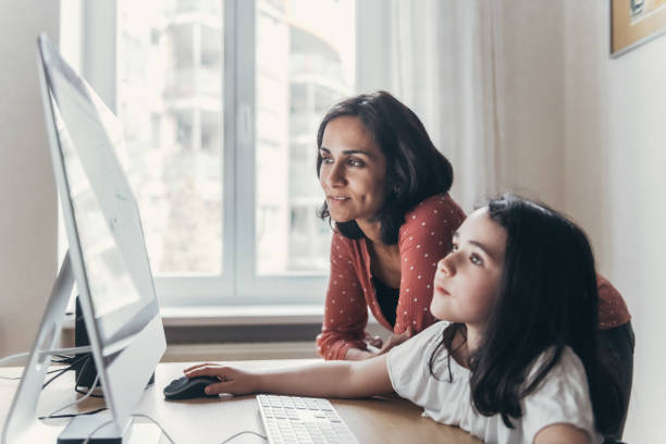 mother and little daughter looking together at computer monitor stock photo