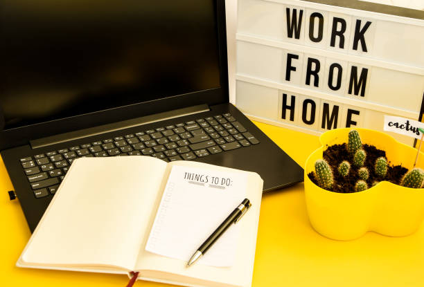 istock Text WORK FROM HOME with notebook, laptop and pen, cactus, work from home place, freelance environment on yellow background copy space 1213483780