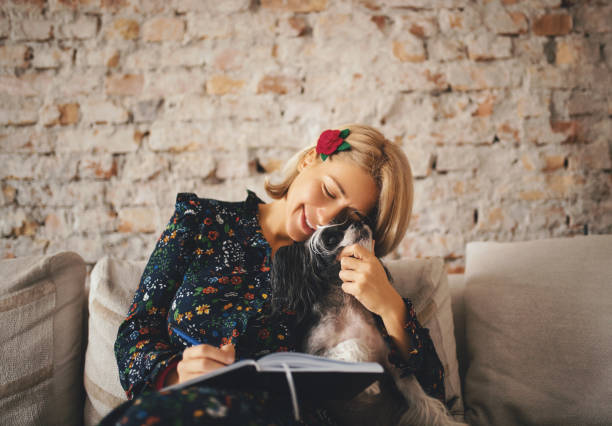 Young woman sitting at home with her dog, cuddling and finishing some work.