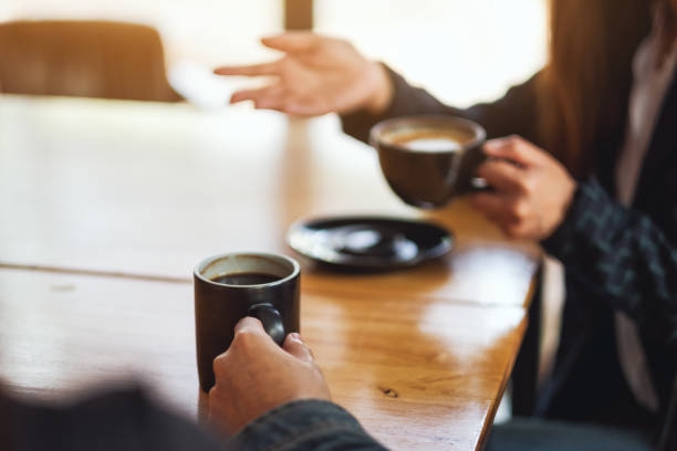 Side view close up of two women hands talking in a bar or house holding coffee cups