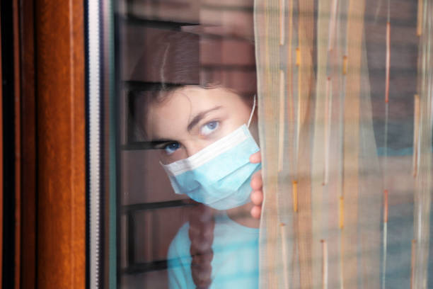 istock Girl wearing a face mask looking through a window 1213492901